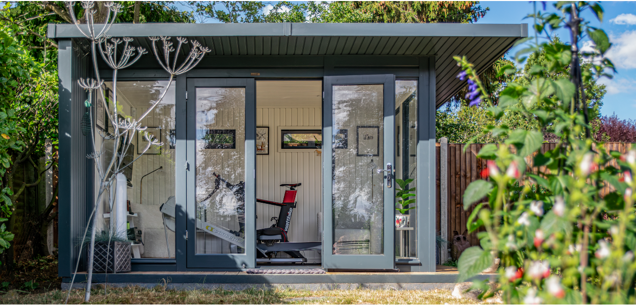 Interior view of Jenny's Crane Holt Studio garden gym featuring a rowing machine, exercise bike, and wall-mounted TV in Cringleford, Norfolk