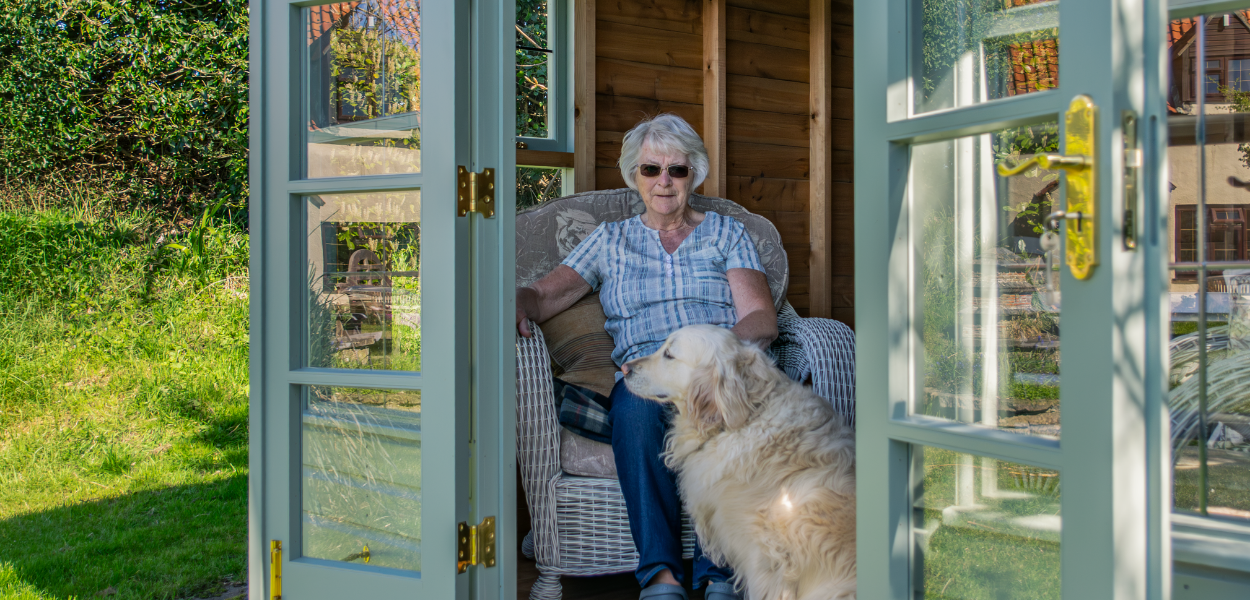 Our customer Vivien and her Golden Retriever sitting inside her Crane summerhouse with the doors open looking out onto the garden.