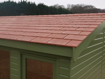 Close-up of a green garden building roof finished with overlapping terracotta slate-effect tiles.