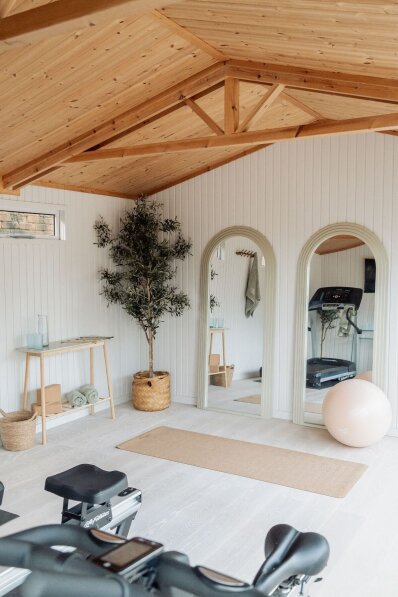 Burnham Studio as a Home Gym / Yoga Studio Bright garden gym interior with white panelled walls, exposed timber roof trusses, exercise bikes, yoga mat, mirrors and fitness equipment.