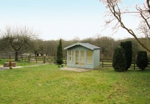 An attractive blakeney summerhouse in a rural location, pictured next to a fence. The building has double doors and large windows as well as an apex roof with slight overhang. 