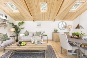 A wide angle interior image of the pavilion garden room with a dining room and relaxing area set up. The roof is visible with three velux windows added and two trusses. 