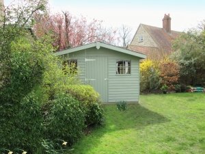 An attractive garden shed nestled in a well-kept garden partially concealed behind shrubbery. The apex roof is covered in heavy-duty felt and has a slight overhang on the gable. 