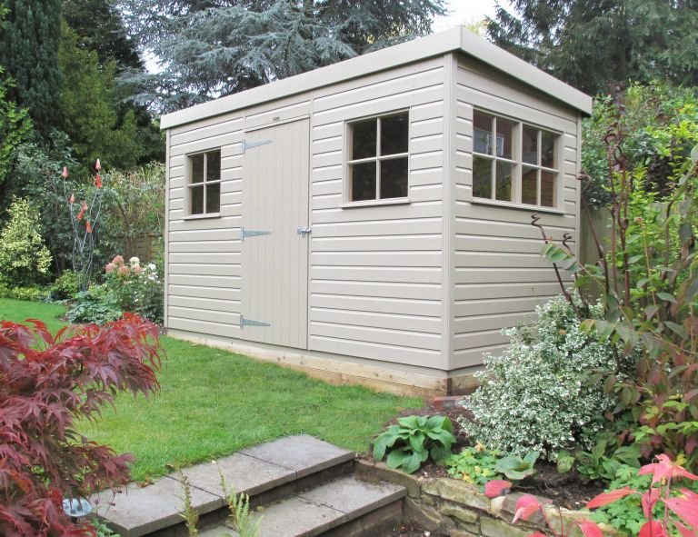 A pent roofed superior shed pictured from a low angle. The building features smooth shiplap exterior cladding and windows with georgian bars. 