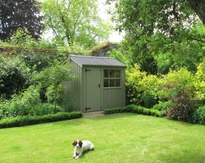 1.8 x 2.4m Felbrigg National Trust Shed painted in Wades Lantern with a dog laying in front of it on the grass