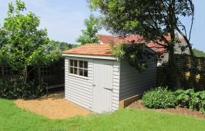 An image showing an apex garden shed covered with cedar shingles and rustic weatherboard cladding. The windows feature georgian bars. 