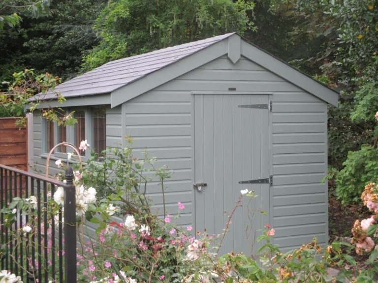   A large superior shed with an apex roof covered in slate tiles and clad with smooth shiplap painted in the exterior shade of pebble. 