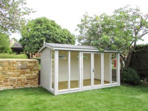 A beautiful garden studio with seven fully-glazed windows and an apex roof covered in slate-composite tiles. The interior is visible through the windows and features painted lining and a lacquered floor. 