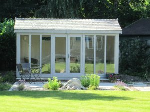 An attractive garden studio positioned in a well-kept garden with an apex roof covered in slate-composite tiles with eight fully-glazed windows. 