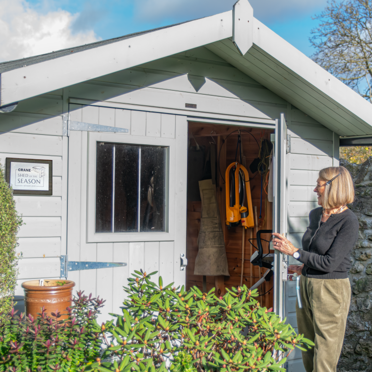 Woman stands next to a shed with open door. A Shed of the Season winner's plaque is on the front of the shed.