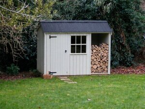 National Trust Blickling Shed with log store. Painted in a light grey and trees in the background.