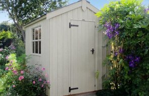 Traditional style garden shed with vertical sawn rustic cladding, Georgian windows, and black corrugated roofing in a English style garden with blossoming summer flowers.